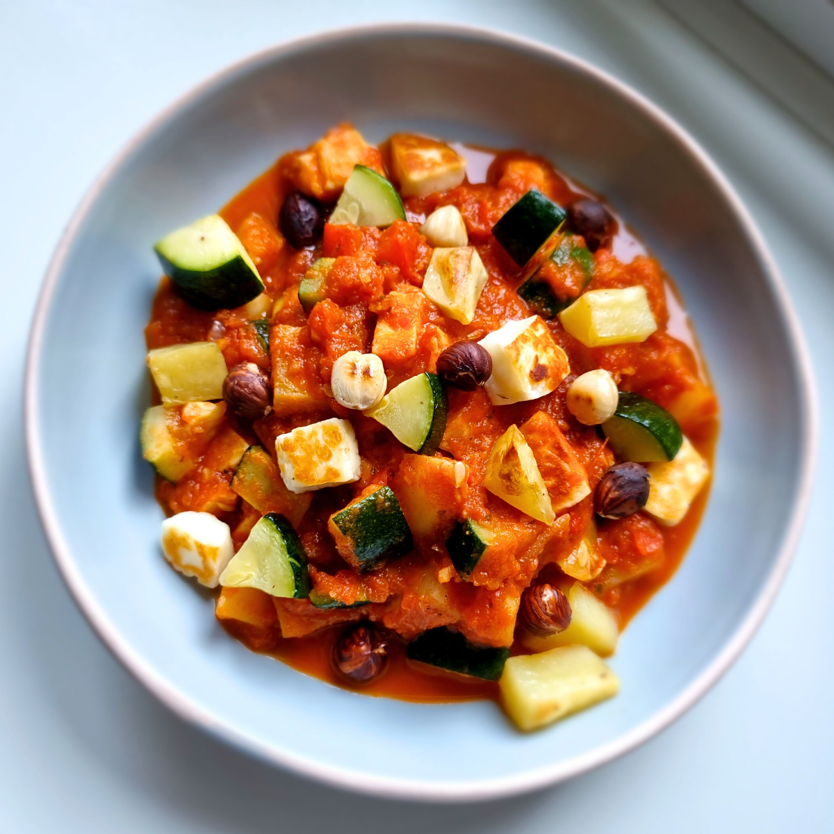 Halloumi in een pikante tomaat- & paprikasaus. Met courgette, aardappel & geroosterde hazelnoten