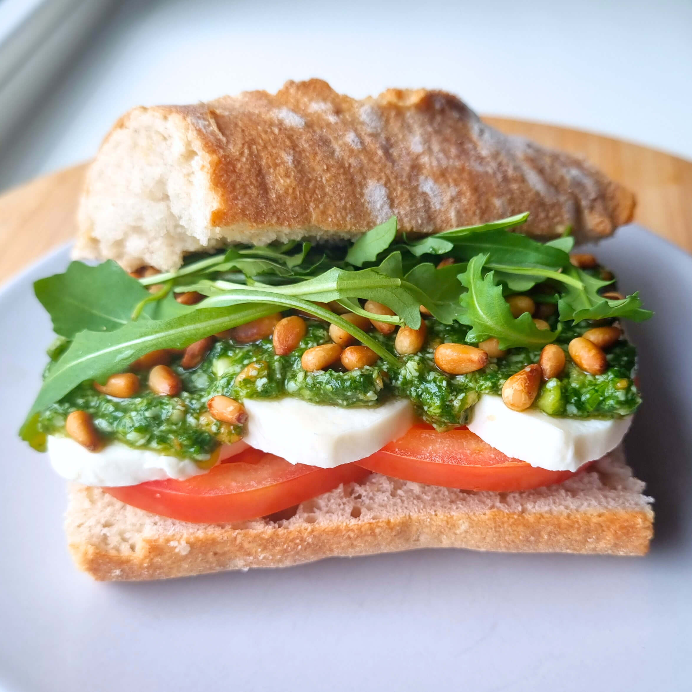 Italiaanse belegde baguette met mozzarella, tomaat, basilicum, rucola, pesto Genovese en geroosterde pijnboompitten