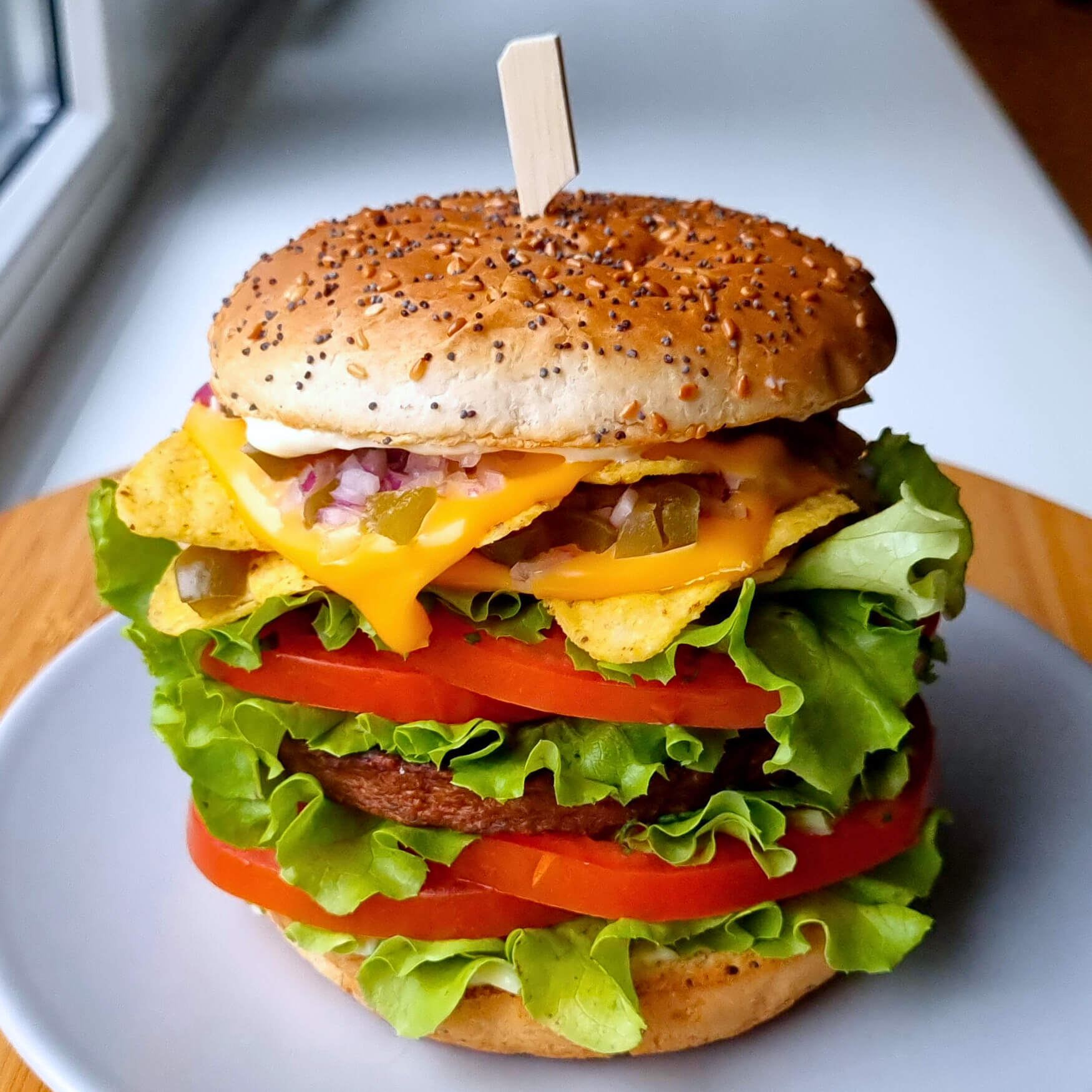 Vega cheeseburger met tortilla chips, jalapeño pepers, rode ui, sla en tomaat