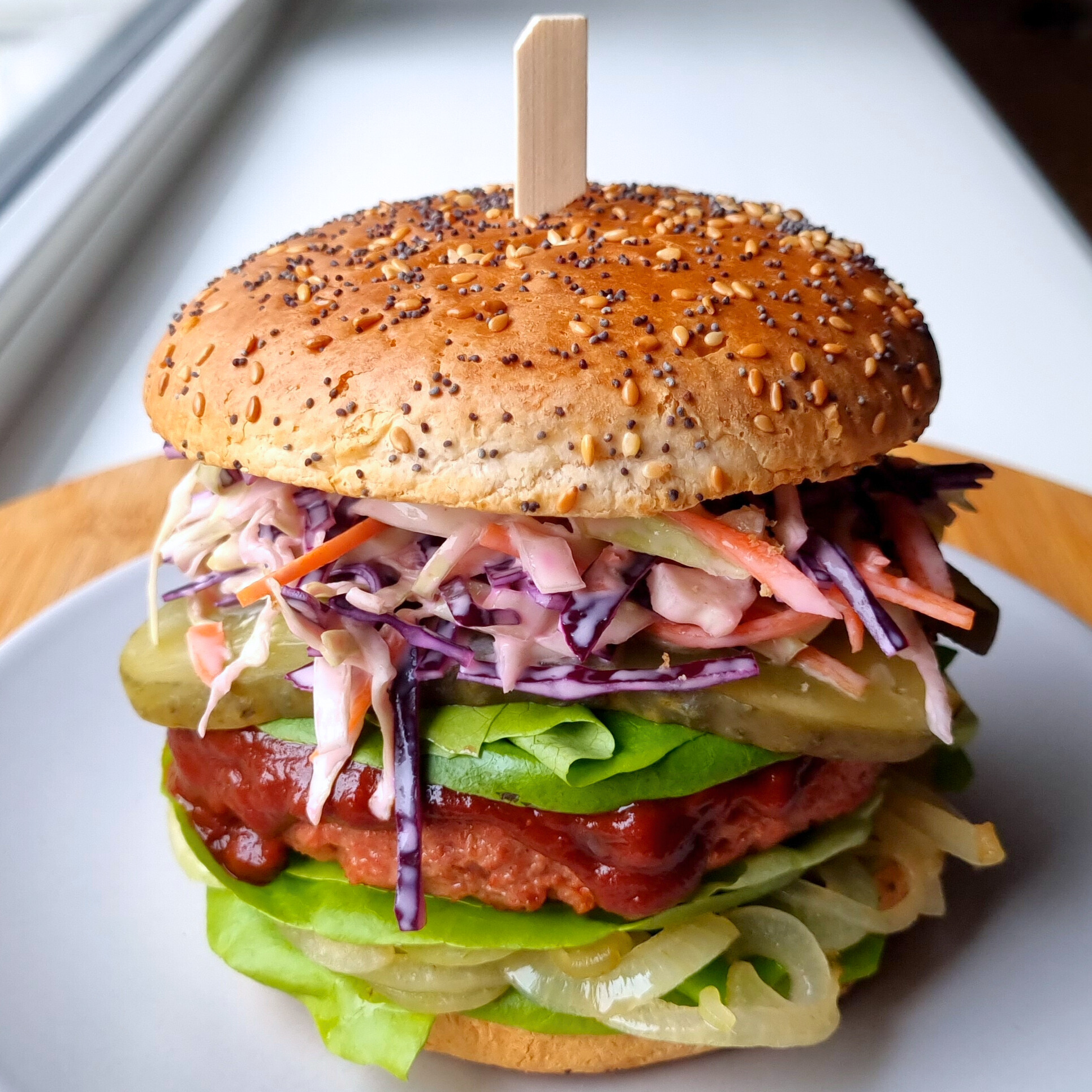 Veganistische hamburger met Amerikaanse coleslaw, BBQ-saus, augurk, kropsla en gebakken ui